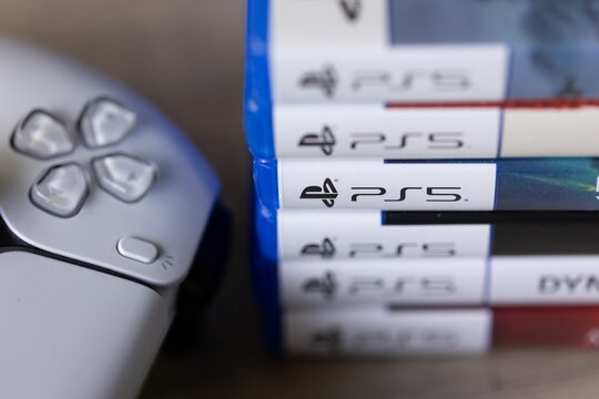 Brecht, Belgium - 18 april 2025: A closeup portrait of a stack of sony playstation 5 videogame cases or boxes next to an original white PS5 wireless controller. Ready to play a console game.