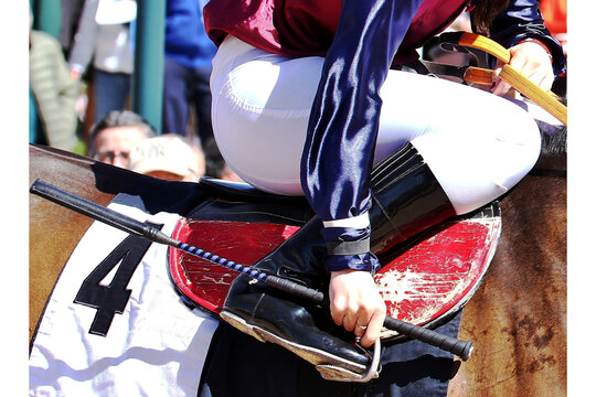 Jockey con l&aacute;tigo y rienda ajust&aacute;ndose el estribo sobre el caballo en el paddock del hip&oacute;dromo como preparativo de la carrera