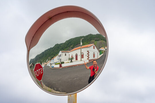 Caucasian European white man dressed in red sweater and camera deformed by concave mirror on background of rural location of Azores, Portugal