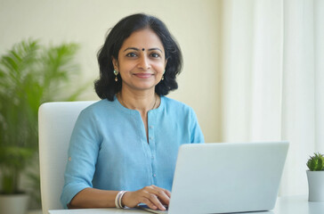 A serene and self-assured Indian middle-aged woman seated at a minimalist white desk with a laptop