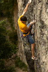 A man in a yellow shirt is climbing a rock wall