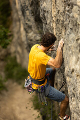 A man in a yellow shirt is climbing a rock wall