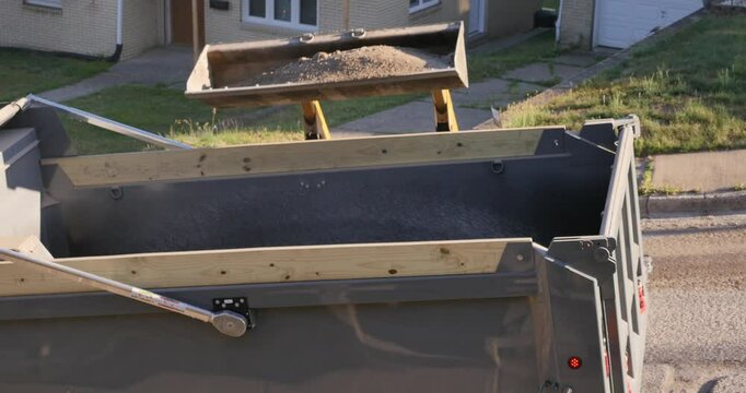 A view of a small backhoe dumping dirt into a truck at a construction site. With audio.  	