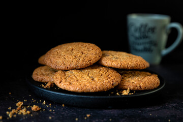 Plate of chocolatechip cookies on a dark background with a cup of coffee