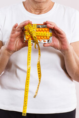 Elderly senior woman with vitamins or supplements and centimeter in hand. Treatment, slimming or strengthening immunity in old age