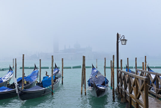 Row of snow and frost covered gondolas near San Marco Square with Chiesa di San Giorgio Maggiore in background. Venice, Italy.
