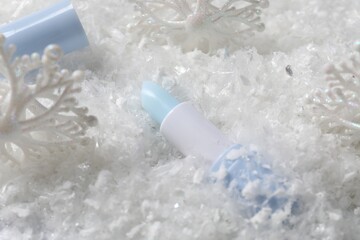 Moisturizing lip balm and Christmas decor on artificial snow, closeup. Winter care