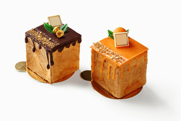 Two small square cakes with chocolate and orange topping resting on golden coasters