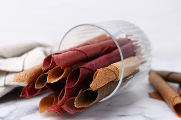 Tasty fruit leather rolls on white marble table, closeup