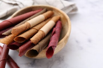 Tasty fruit leather rolls on white marble table, closeup