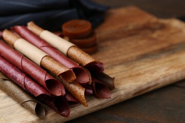 Tasty fruit leather rolls on wooden table, closeup