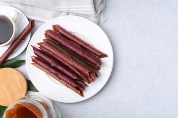 Tasty fruit leather rolls and tea on white table, flat lay. Space for text