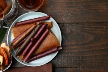 Tasty fruit leather rolls and tea on wooden table, flat lay. Space for text