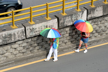 Couple walking with rainbow umbrellas next to a wall. LGBTQ