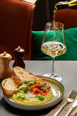 Waiter pouring white wine into glass with gourmet hummus, calamari, and bread
