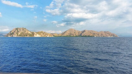 Obraz premium Beautiful sea views with blue water stretching to a dry and hilly landscape with islands in the distance, located in the Komodo National Park area. 