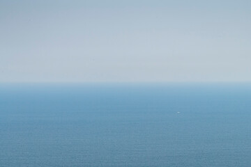 Fototapeta premium White and blue horizontal gradient abstract as a background which is the diffused sky with horizon changing into the blue sea with the tiniest of boats in the water