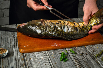 A person skillfully handles a whole fish on a wooden cutting board, using a knife and fork to...