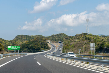 Drivers perspective view over Hanwa Expresway E42 in Wakayama, Japan with exit sign to Gobo Minami (translates in Japanese on sign) and upcoming tunnels through mountains
