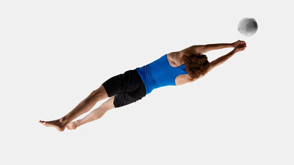 Energetic man, volleyball player reaches forward mid-air with focused eyes on flying volleyball against white studio background. Aerial view photo. Concept of training, sport events, game, goal