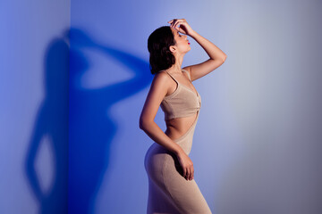Glamorous young woman posing in stylish beige dress against artistic blue and white studio...