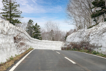 Obraz premium Driver perspective view of road National Route 103 lined with walls of snow from Aomori, Japan, towards Mount Hakkoda in early spring with white clouded blue sky