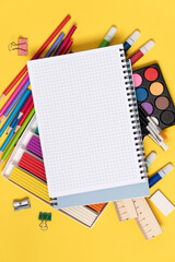 Notebook sheet with free space for text and education supplies behind it -  pencils, markers, plasticine, rulers, erasers. Back to school, creativity, study concept yellow background with copy space