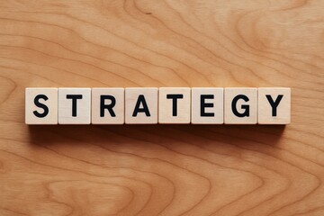 An overhead view wooden blocks arranged to spell strategy on a maple desk symbolizing business decision-making and planning