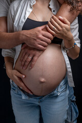 A pregnant woman is hugged from behind by her man while holding her belly with one hand