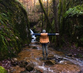 young man meditating happily opening his arms to nature in front of small waterfall in nature in...