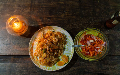 Seafood pasta dish with coconut sauce and salad served on a wooden table in a romantic and peaceful setting with candlelight