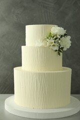 Delicious wedding cake with floral decor on table against grey background