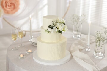 Delicious wedding cake with floral decor and glasses of champagne on table indoors