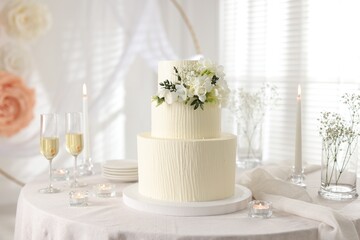 Delicious wedding cake with floral decor and glasses of champagne on table indoors