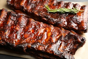 Tasty roasted pork ribs served with rosemary on table, closeup