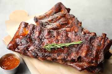 Tasty roasted pork ribs served with rosemary and sauce on light grey table, closeup