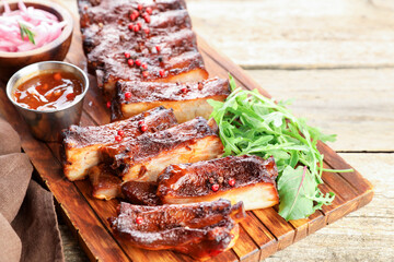 Delicious spare ribs, sauce and arugula on wooden table, closeup