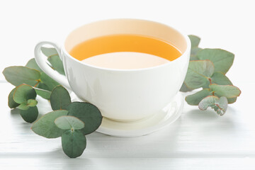 Aromatic tea in cup and eucalyptus branches on white wooden table, closeup