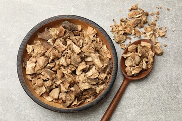 Pieces of dry chicory roots in bowl and spoon on gray textured table, flat lay