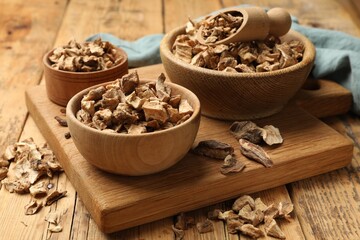 Pieces of dry chicory roots in bowls and scoop on wooden table