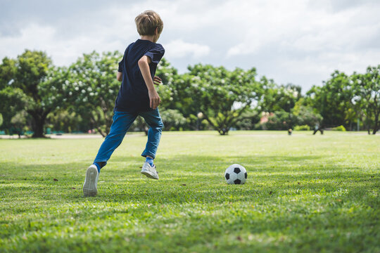 Little boy playing football in the garden with morning sunrise