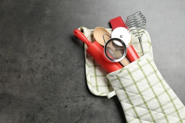 Different kitchen utensils in oven mitten on grey table, top view. Space for text