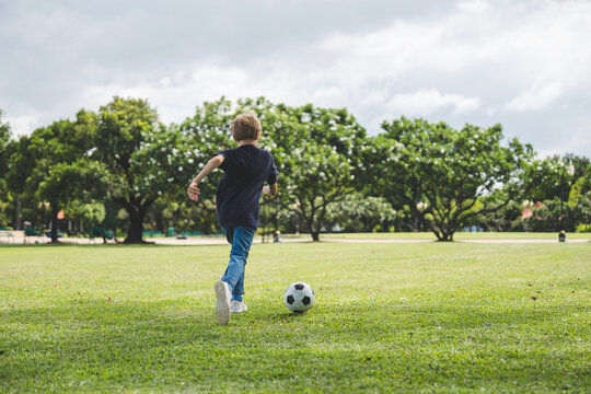 Little boy playing football in the garden with morning sunrise