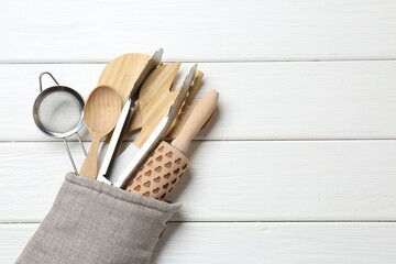 Different kitchen utensils in oven mitten on white wooden table, top view. Space for text