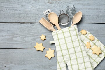 Different kitchen utensils in oven mitten and star shaped cookies on light grey wooden table, flat...