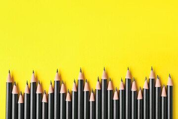 Many sharp graphite pencils on yellow background, flat lay. Space for text