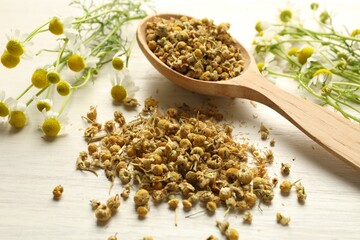Dry, fresh chamomile flowers and spoon on light wooden table, closeup