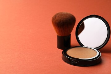 Open face powder with mirror and brush on coral background, closeup. Space for text