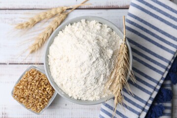 Wheat flour in bowl, grains and spikes on light wooden table, flat lay