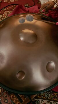 Vertical shot of Hands of young unrecognizable African American female musician using drumsticks to beat metallic surface of ethnic glucophone while creating new music